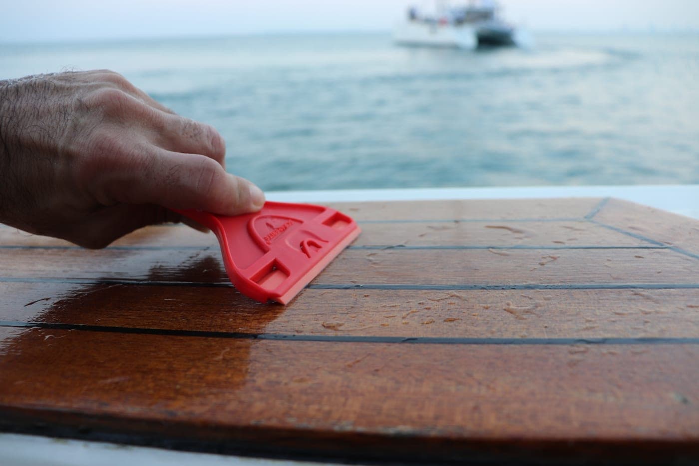 Scraperite Hand Using Red Scraper On Wooden Surface