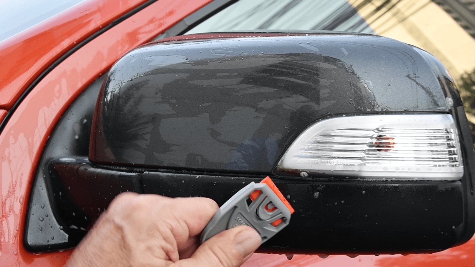 Hand using Scraperite Razor Scraper to clean a car side mirror